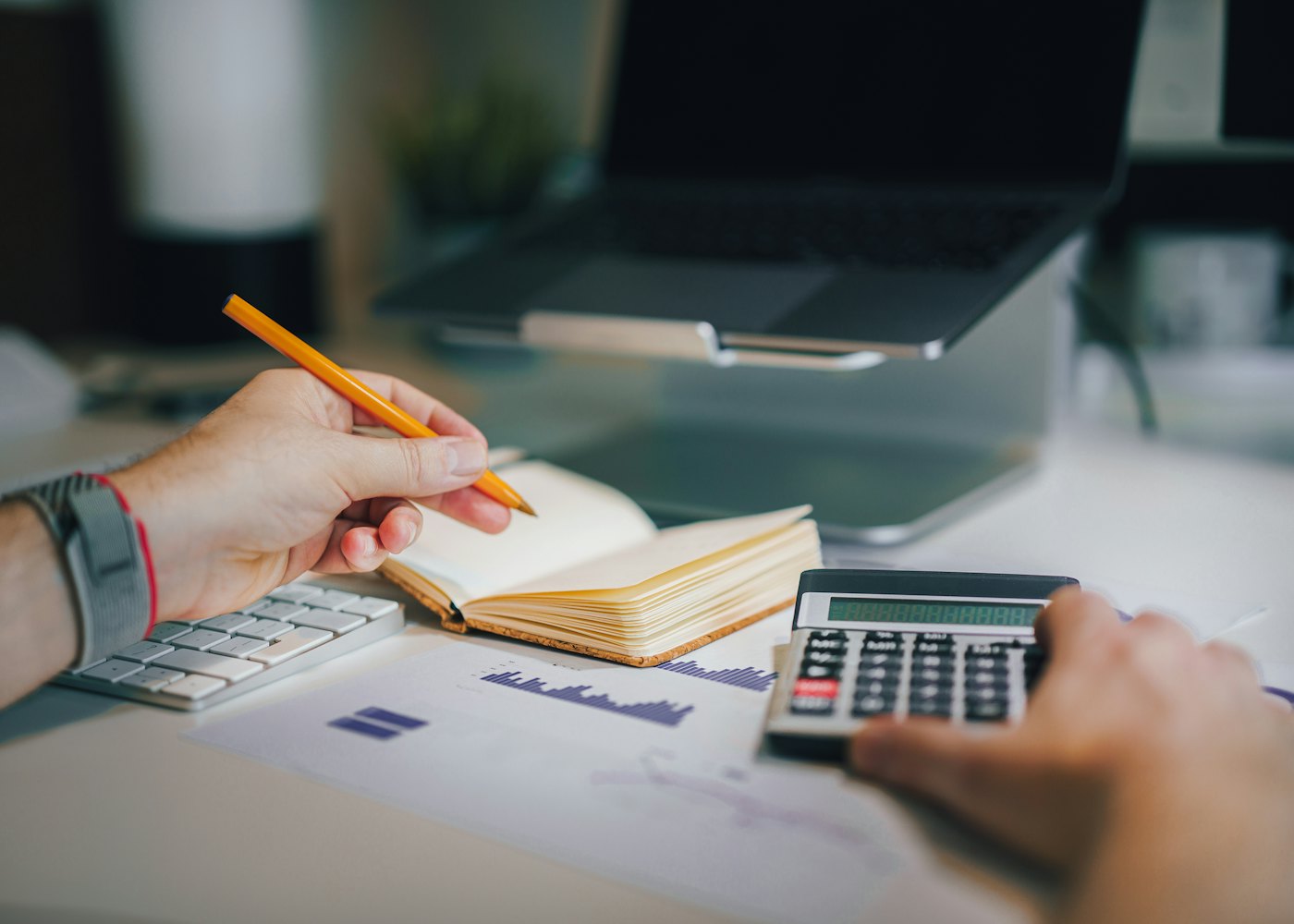 Bookkeeper recording entries in a ledger with a calculator and financial reports