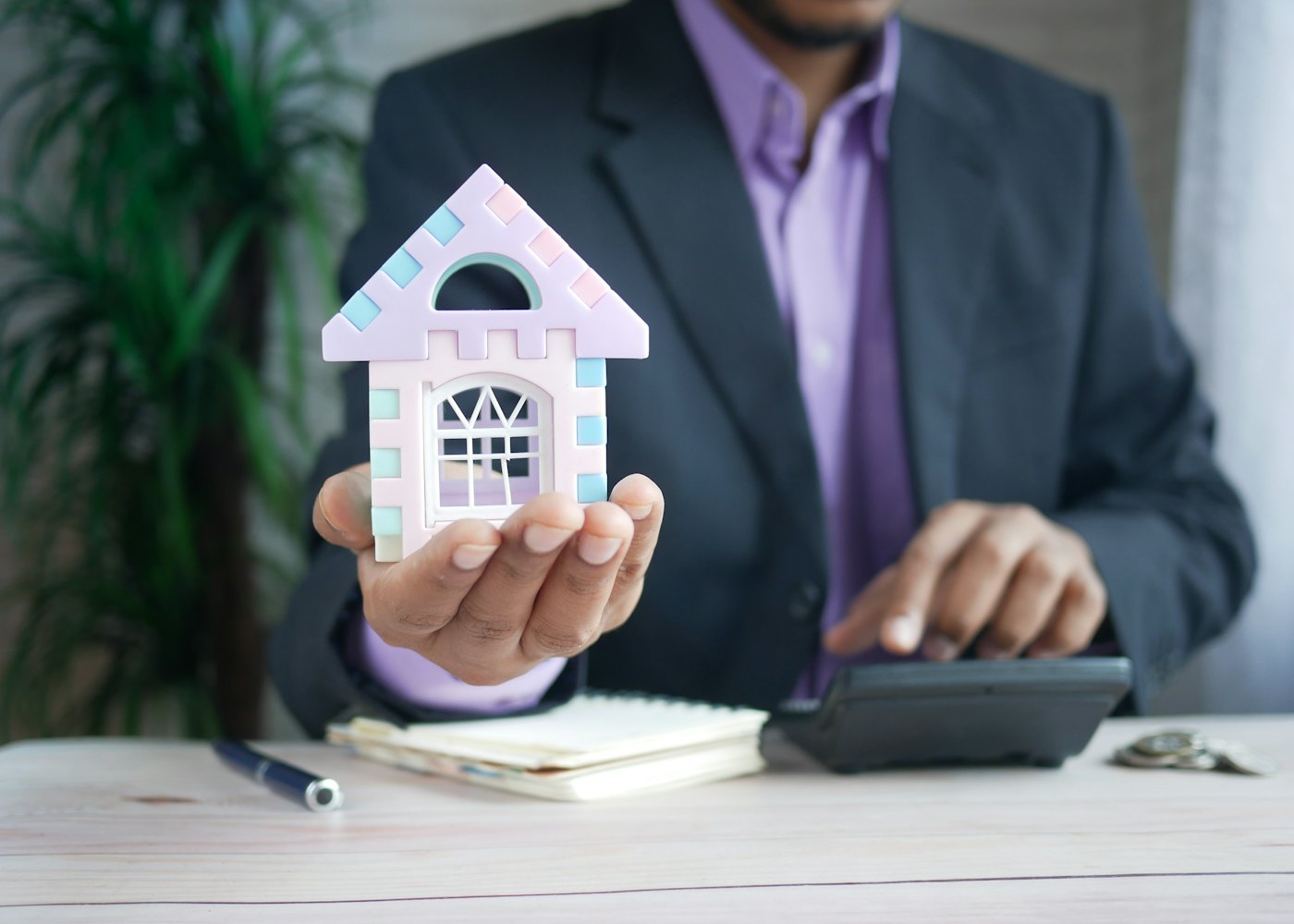 Real estate investor holding a model house at a desk with a calculator